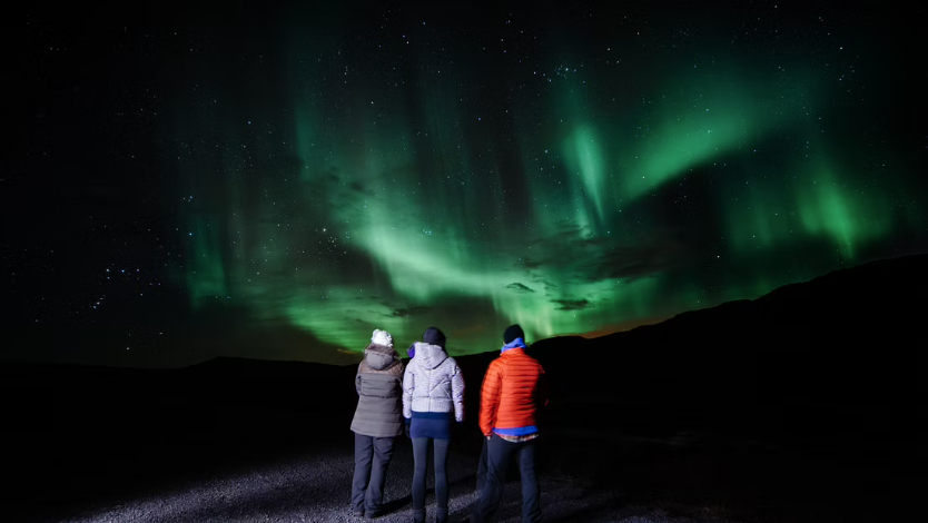 Tourists observing green northern lights on a patchy sky