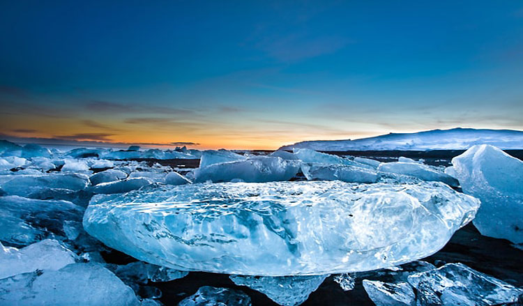 Close up of a fragment of iceberg on the black sand on the lagoon shore at sunset.