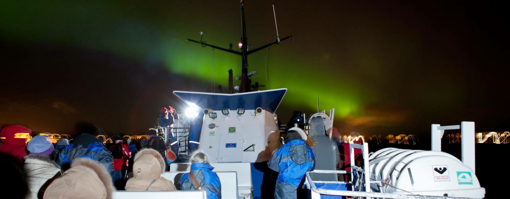 Bunch of tourists gathered on the deck of the cruise ship, observing the northern light display
