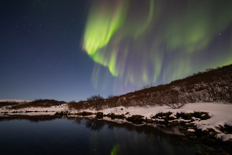 Green northern lights dancing in the night sky over a lake and the snowy shore