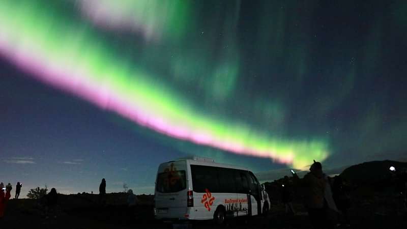 Three people with cameras and tripods watch the northern lights dance in the night sky