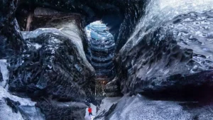 A visitor exploring the black and blue ice inside the ice cave under the volcano