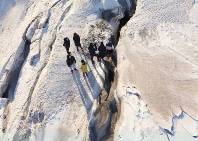 Individuals in winter outdoor clothes line up to enter an ice cave through a crevasse on langjökull glacier