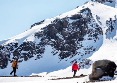 Two individuals in winter outdoor clothes walk on a glacier on a sunny day