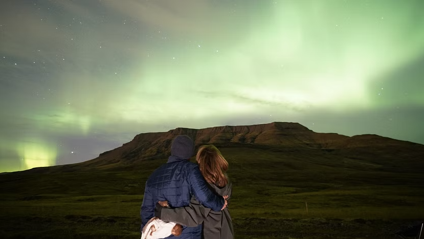 Enamoured couple contemplating the northern lights over a mountain in the countryside