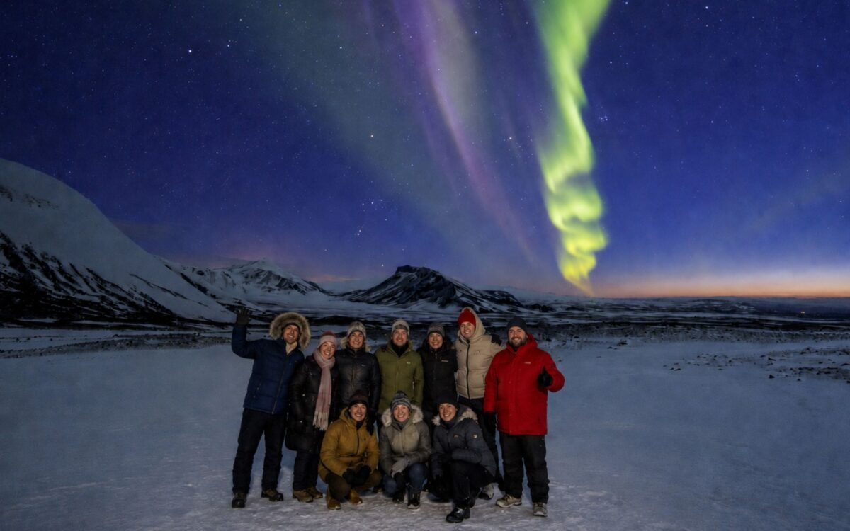 A group of guests posing under the Northern Lights on a small group tour with Aurora Reykjavík in Iceland