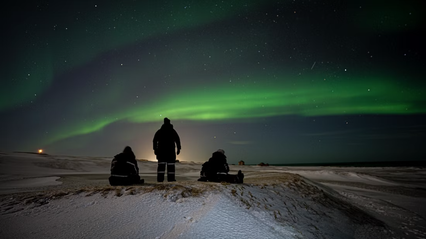 Tourists sitting and watching the northern lights from the countryside on a snowy landscape