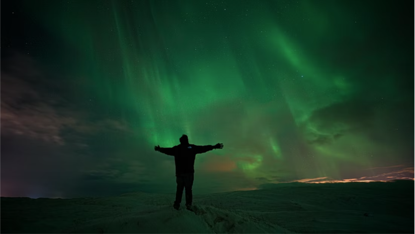Tourist posing for a picture with northern lights in the background