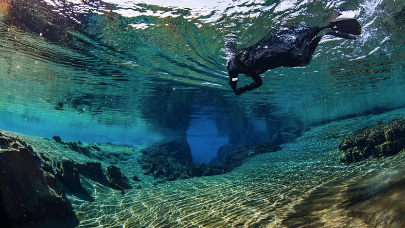 Tourists Snorkeling in crystal clear waters between the continents in Silfra: underwater view