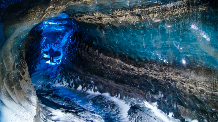 Visitor exploring the natural Katla ice cave, with its typical blue and black icy walls.