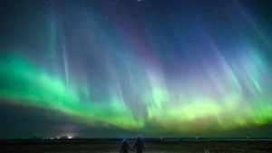 Two people holding hands while watching northern lights in green and purple lighting up the night sky