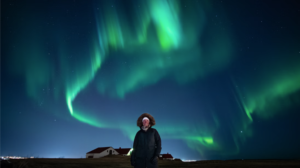 A woman posing for a picture while the northern lights dance in the sky above