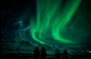 Travellers watching the northern lights dance over the mountains